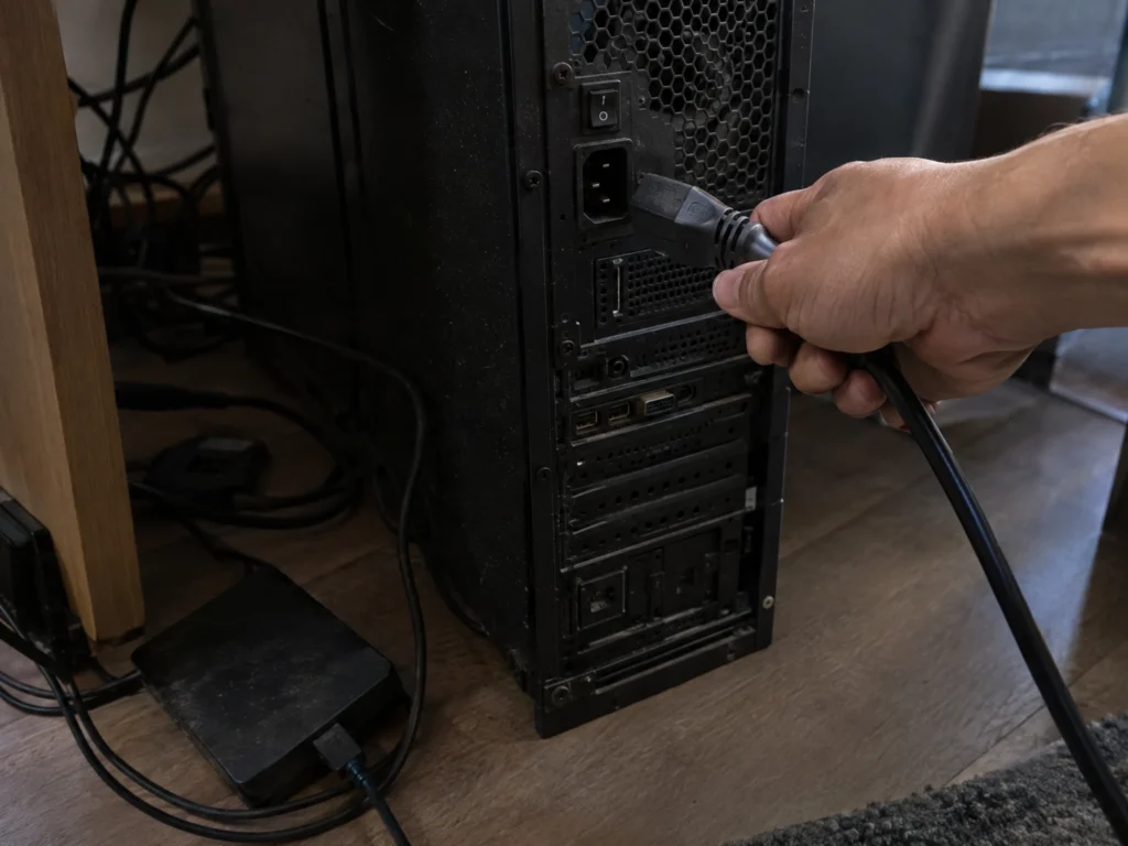 Mão desconecta o cabo de energia de um computador de mesa, ao lado de um HD externo